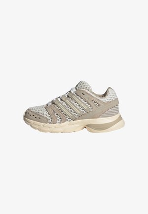 Baskets de sport en mesh beige et blanc avec semelle rembourrée, lacets à l'avant et renforts de soutien, conçues pour la course ou un usage décontracté.