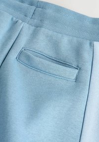 Pantalon de survêtement bleu clair en tissu doux et texturé, avec une taille élastique et une petite poche rectangulaire à l'arrière.