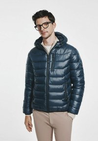 Granatowa kurtka puchowa z kapturem, z wzorem pikowanym, zapinana na zamek, z gładkimi, błyszczącymi elementami. Lekka i izolująca.