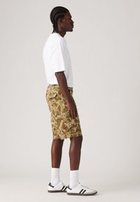 White short-sleeve t-shirt paired with khaki camo cargo shorts. Outfit completed with white sneakers and crew-length white socks.