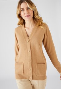 Cárdigan de punto beige con escote en V, cinco botones y dos bolsillos delanteros; presenta puños y dobladillo de canalé, textura suave y diseño ligero.