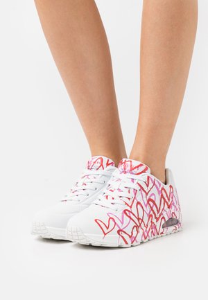 Witte sneakers met een patroon van rode en roze hartvormen; textuur van de bovenkant, vetersluiting aan de voorkant en een gevoerde zool.