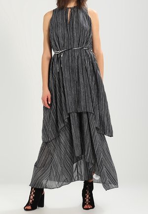 Schwarz-weiß gestreftes Maxikleid mit ärmellosem Design, Schlüsselloch-Ausschnitt, tailliertem Bund und asymmetrischem Saum; kombiniert mit schwarzen Absatzsandalen.