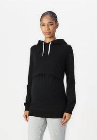 Black hoodie with a cropped design, drawstring, and long sleeves. Paired with light grey tapered pants for a casual look.