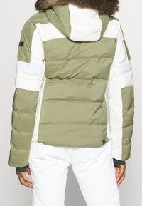 Giacca puffo con una combinazione di colori verde e bianco; presenta un cappuccio con bordo in pelliccia sintetica, design trapuntato e polsini elasticizzati.
