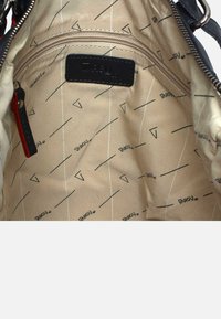 Geverfde beige binnenkant van een tas met een ritsvak, merkreclame en geometrische patronen met zwarte lijnen en vormen.