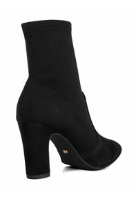 Black ankle boot made of suede with a slim, curved heel and pointed toe. Features seamless design and subtle gold accent on the heel.
