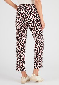 Pantaloni neri con un motivo vorticoso rosso e bianco, vita elastica, taglio dritto e lunghezza cropped, abbinati a scarpe chiare.