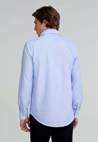 Camicia azzurra a maniche lunghe con colletto a punta, orlo curvo e polsini abbottonati. Realizzata in un tessuto morbido con una trama sottile.