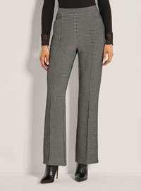 Vrouw in een zwart-wit gestreepte broek met hoge taille en wijde pijpen, met zwart puntig hakken enkellaarzen en een zwart shirt met kant in de mouwen.