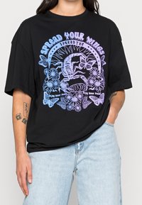 Camiseta de algodón negra con corte oversized, que presenta un gráfico colorido de flores, mariposas y un escorpión junto con elementos textuales.