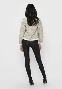 Blouson aviateur à motif floral avec poignets et taille élastiques, associé à un pantalon en cuir noir ajusté, sur un fond neutre.