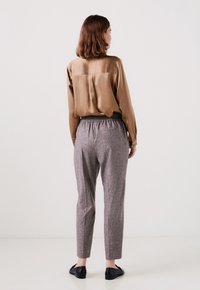Bruin zijden blouse met een ontspannen pasvorm en een plooitje aan de achterkant, gecombineerd met grijze, gestructureerde, taps toelopende broek met een elastische tailleband en zijzakken.