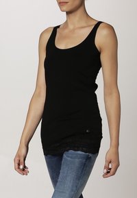 Zwart tanktop met een ronde halslijn, een getailleerde pasvorm en kantafwerking aan de onderrand. Glad katoenmateriaal, minimale hardwaredetails.