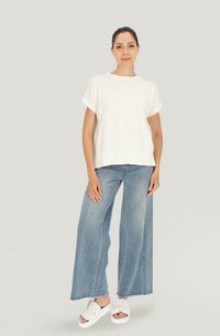 Biała dzianinowa bluzka z krótkimi rękawami i okrągłym dekoltem, zestawiona z jasnoniebieskimi spodniami o szerokich nogawkach i białymi klapkami.