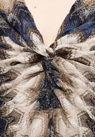 Μπλε, καφέ και λευκό υφασμάτινο μοτίβο, δεμένο σε κόμπο πάνω σε γυμνό δέρμα στο πάνω μέρος του στήθους ενός ατόμου.