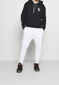 Svart luvtröja med Nike-logotyper, vita dragsnören; kombinerad med vita cargobyxor och svarta sneakers med röda detaljer.