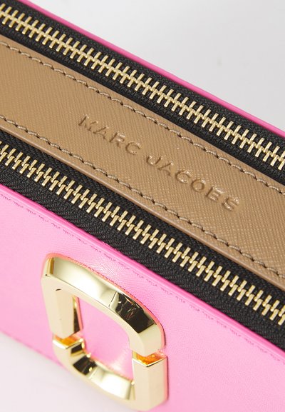 Geantă sintetică roz cu accente aurii, textură netedă și un fermoar contrastant de culoare bej. Prezintă logo-ul debrosat "MARC JACOBS" pe un panou bej.