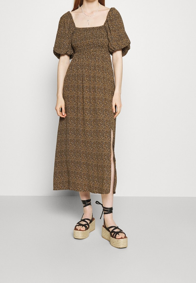 Brun blommig maxiklänning med puffärmar och fyrkantig halsringning. Har en sidssprund. Bärs med svarta remsandaler med plattform.