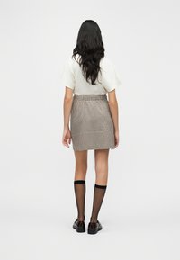 Μαύρη και λευκή μίνι φούστα με καρό μοτίβο και σούρα στη μέση, σε συνδυασμό με μαύρες κάλτσες μέχρι το γόνατο και μαύρα παπούτσια, από πίσω όψη.