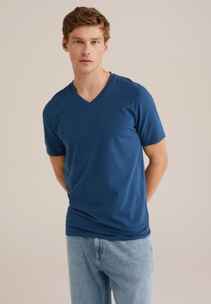 T-shirt bleu marine à col en V en tissu doux, avec des manches courtes et une coupe décontractée, associé à un jean en denim bleu clair.