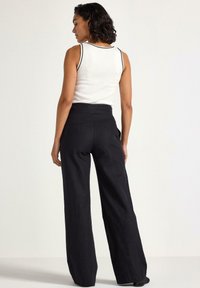 Pantalons noirs à large jambe avec une taille haute et une finition en tissu lisse, associés à un débardeur blanc avec des bordures noires.