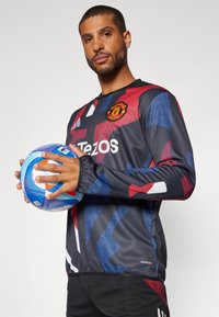 Maglia da calcio nera con motivi astratti rossi e blu, con colletto rotondo, maniche lunghe e dettagli del logo; tenuta con una palla multicolore.