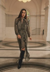 Rochie maxi cu model negru și bej, cu mâneci lungi, volane și decolteu în formă de cheie, asortată cu cizme negre până la genunchi.