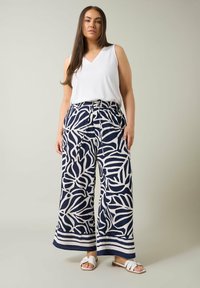 Top blanco sin mangas combinado con pantalones anchos de rayas marinos que presentan un diseño de hojas y cintura con cordón. Sandalias blancas completan el look.
