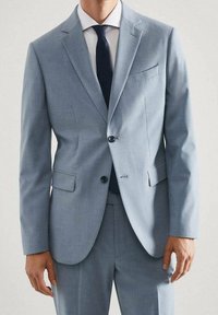 Costume bleu clair présentant un design ajusté, une veste à un bouton avec deux boutons, des revers en pointe et une poche poitrine. Tissu texturé.