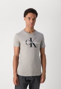 Pelēks kokvilnas t-krekls ar apaļu izgriezumu, īsām piedurknēm, ar lielu melnu "CK" logo un baltu uzrakstu "Calvin Klein Jeans".