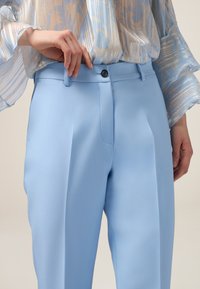 Hellblaue, taillierte Hosen mit glatter Textur, ausgestattet mit einem Bund mit Knopfverschluss und vorderen Falten.