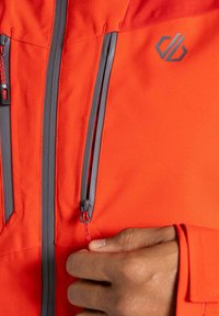 Helle orange Jacke mit grauen Reißverschlüssen und Akzenten. Verfügt über zwei Reißverschluss-Taschen und detaillierte Nähte. Weicher, texturierter Stoff.