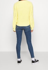 Pull en maille jaune avec un col rond et un motif texturé en tricot lâche. Assorti à un jean skinny bleu et des baskets noires.