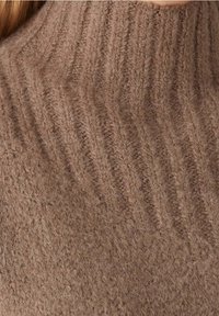 Brauner gerippter Strickpullover mit hohem Kragen. Die Textur ist weich und flauschig, mit auffälligen vertikalen Mustern.