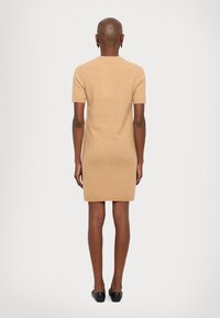 Knit, short-sleeve, beige dress with a straight cut. Features a round neckline and soft texture. Worn with black flats.
