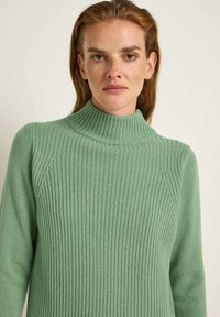 Hellgrüner Rollkragenpullover mit vertikaler Rippung, taillierter Passform und strukturiertem Stoff. Lange Ärmel und hoher Halsausschnitt.