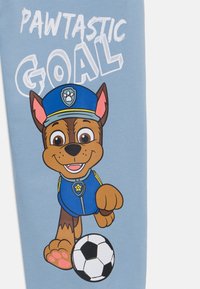 Zils audums ar multfilmas suni policista tērpā, tur rokās futbola bumbu. Teksts lasāms "PAWTASTIC GOAL" treknās baltās burtos.