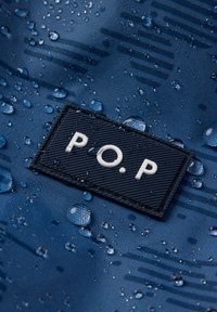 Nærbillede af vanddråber på blåt stof med et sort rektangulært logo-udsnit, der har teksten "P.O.P" i hvide bogstaver.