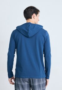 Langermet hette jakke i mørk blått stoff, med en glatt tekstur og minimalistisk design. Sammen med rutete bukser.