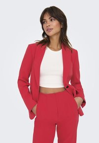 Veste rouge cintrée et pantalon taille haute assorti par-dessus un crop top blanc. Tissu lisse avec un design structuré et une coupe ajustée.