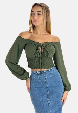 Top verde scollato con scollo arricciato e vita aderente, abbinato a una gonna di jeans a vita alta. Maniche lunghe, design casual.