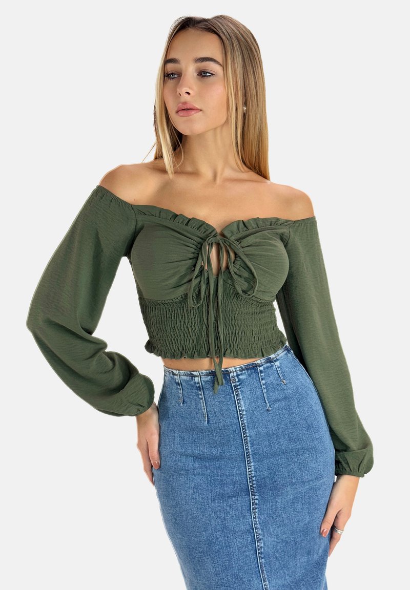Top verde scollato con scollo arricciato e vita aderente, abbinato a una gonna di jeans a vita alta. Maniche lunghe, design casual.