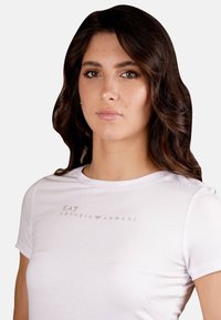 T-shirt bianco a maniche corte realizzato in morbido cotone, con un sottile logo EA7 Emporio Armani in grigio chiaro sul petto.