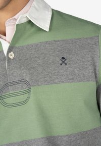Groen en grijs gestreept poloshirt met een witte kraag, voorzien van een klein geborduurd logo en zichtbare stiksels aan de linkerkant.