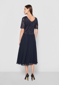 Abito navy con bustier in pizzo, maniche corte e gonna svasata. Tessuto testurizzato e design con scollatura a V sul retro. Abbinato a scarpe nere con tacco.