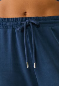 Hosen aus marineblauem elastischem Material mit einem Kordelzug. Der Kordelzug hat metallische Enden. Glatte Textur, mit Fokus auf dem oberen Bereich des Kleidungsstücks.