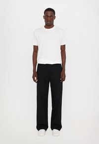 T-shirt en coton blanc à col rond, associé à un pantalon noir ample et des baskets blanches. Design simple et couleurs classiques.