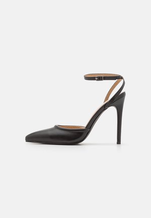 Chaussure à talon haut en cuir noir avec un bout pointu, des côtés ouverts et une bride à la cheville. Présente une texture lisse et élégante ainsi qu'un talon fin.