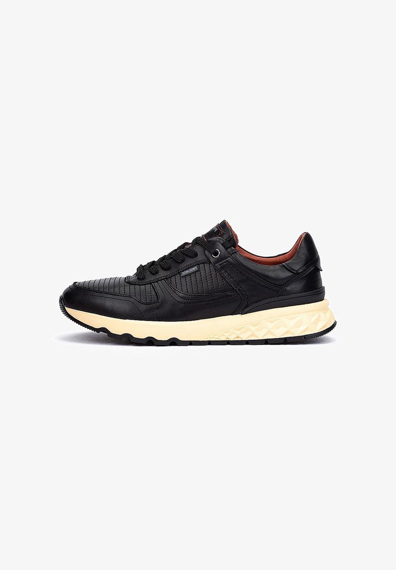 Zapatilla negra de cuero con parte superior texturizada, puntera redonda y entresuela color crema. Presenta cordones negros y una suela de goma con un patrón geométrico.